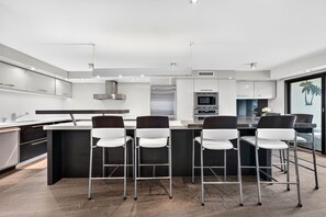 A modern kitchen with a central island, bar stools, stainless steel appliances, and a large window. - The Wavefront | Gulf-front Executive Residence (St. Pete Beach)