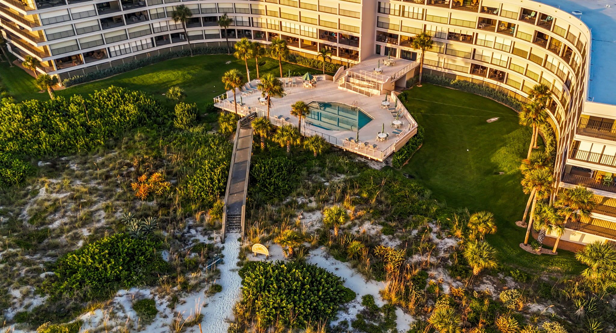 Ein Hochhotel mit mehreren Balkonen, einem Schwimmbad und einer angelegten Gartenanlage.