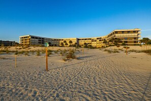 A beachfront hotel with multiple floors, a sandy beach in the foreground, and a clear sky. - The Wavefront | Gulf-front Executive Residence (St. Pete Beach)