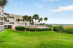 A hotel with a curved building, a well-maintained lawn, palm trees, and a view of the ocean. - The Wavefront | Gulf-front Executive Residence (St. Pete Beach)