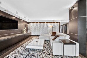 A modern living room with a white sofa, a coffee table, and a TV on the wall. - The Wavefront | Gulf-front Executive Residence (St. Pete Beach)