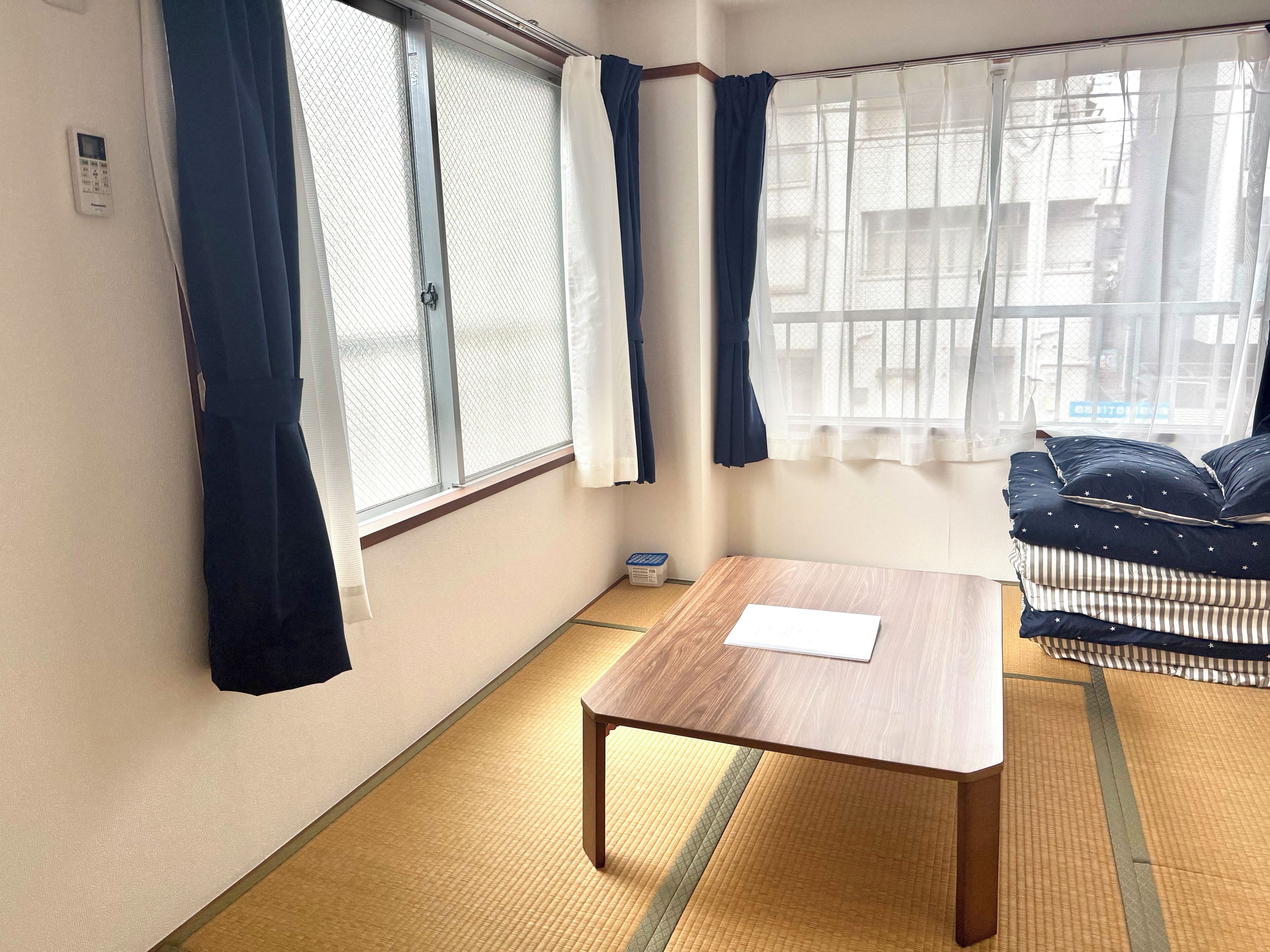 A room with a wooden table, a sofa with patterned cushions, and a window with curtains.