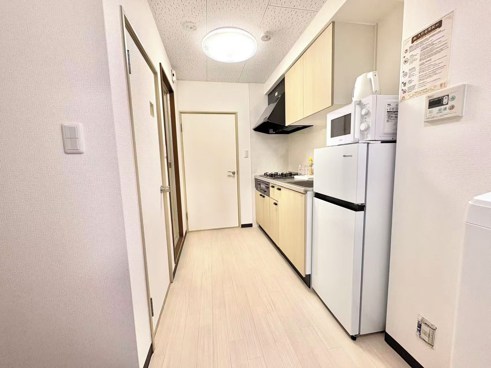 Un couloir étroit qui mène à un coin cuisine équipé d’une cuisinière, d’un four à micro-ondes et d’un réfrigérateur.