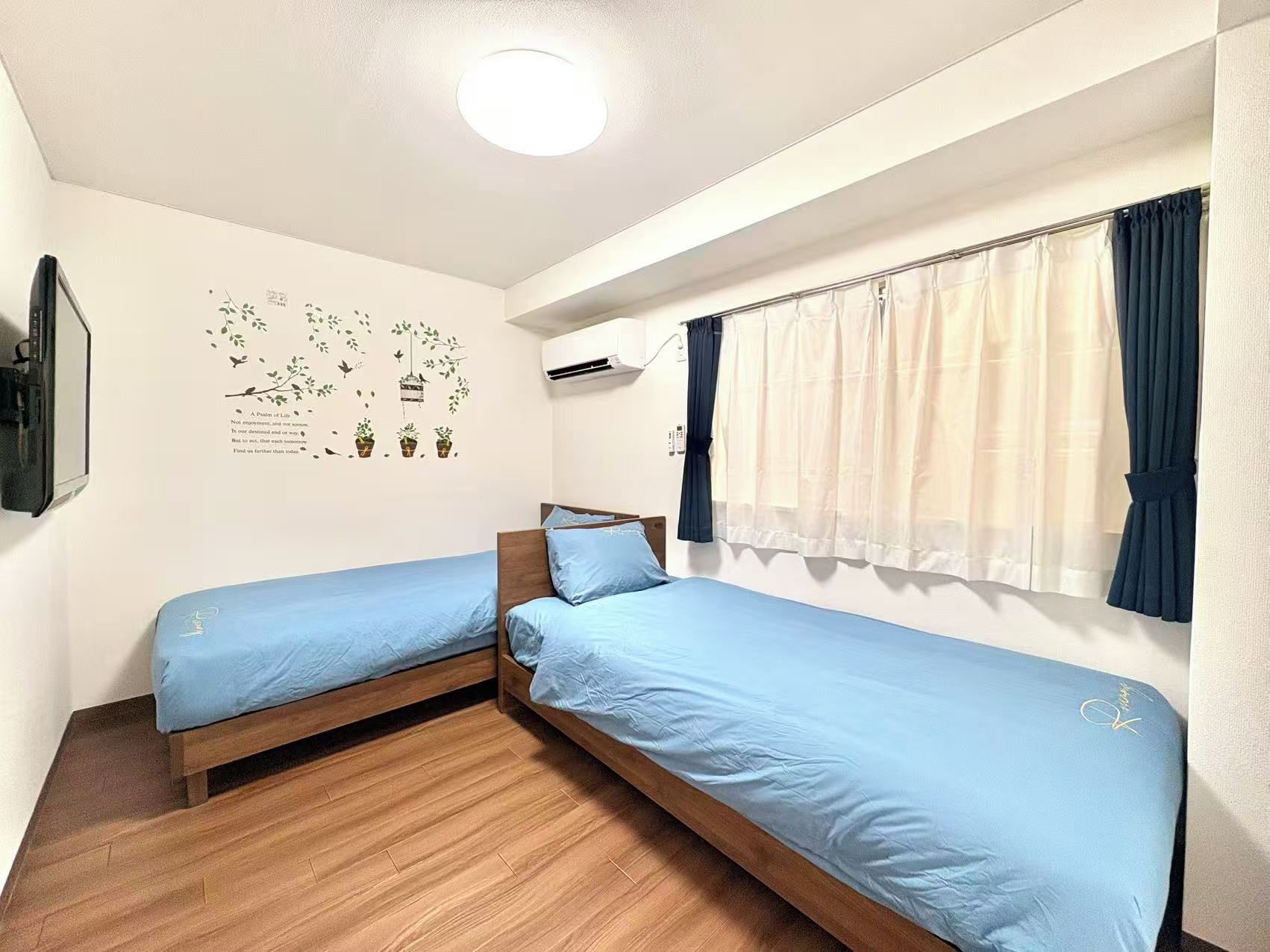 Habitació amb dos llits individuals, una làmpada al sostre, aire condicionat i una finestra amb cortines.