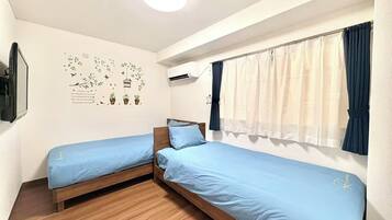 Habitació amb dos llits individuals, una làmpada al sostre, aire condicionat i una finestra amb cortines.