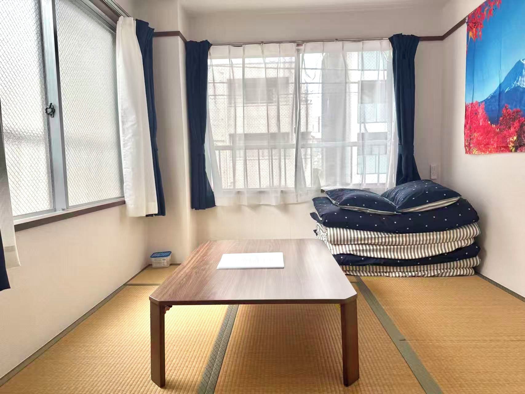 A room with tatami flooring, a wooden table, a sofa with patterned cushions, and a painting on the wall.