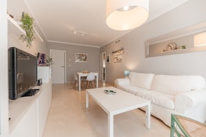 A modern living room with a white sofa, a coffee table, a TV, and a dining area with a table and chairs. - 01 Padel & BBQ Penthouse by Abarzo (Marbella)