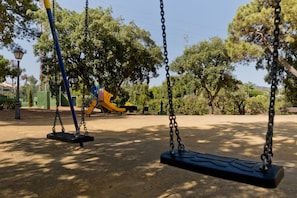 A park with swings, a yellow slide, and trees. - 01 Padel & BBQ Penthouse by Abarzo (Marbella)