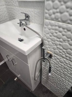 Un baño con un lavabo blanco, un cabezal de ducha de mano y una pared con textura.