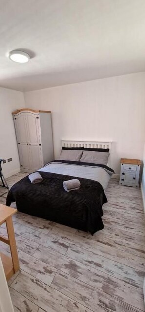 Un dormitorio con una cama, un armario, una mesita de noche y una mesilla.
