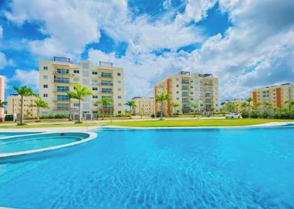 A swimming pool with a clear blue sky and multi-story buildings in the background. - Cozy 1-bedroom apartment with pool and AC in gorgeous Punta Cana (Punta Cana)