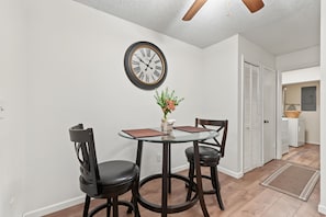 A dining area with a round table, two chairs, a wall clock, and a door leading to a laundry room. - Cozy 2-bedroom house in welcoming Seminole with AC (Seminole)