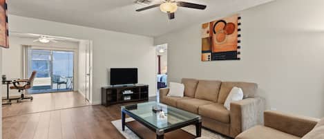 A living room with a sofa, coffee table, TV, and ceiling fan.