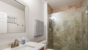 Et badeværelse med en hvid vask, et spejl, et toilet og en brusekabine med glasvægge.