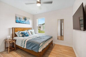 Ein Schlafzimmer mit einem hölzernen Bett, einem Nachttisch, einem Deckenventilator, einem Fenster und einem großen Spiegel.