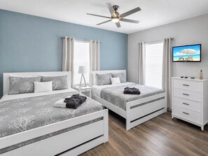 Une chambre avec deux lits, un ventilateur de plafond, une télévision et une commode.