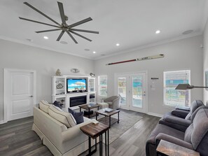 A modern living room with a ceiling fan, a flat-screen TV, and a fireplace. - Mer Sea, 4 bedroom 2.5 bath home sleeps 13. A short stroll to the beach. (Crystal Beach)