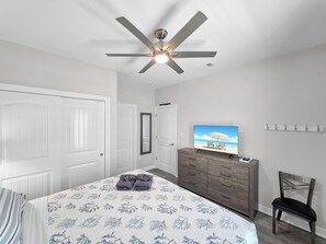 Quarto com cama, penteadeira, televisão e ventilador de teto.