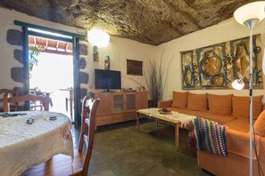A cozy living room with a television, a sofa, a coffee table, and a dining area with chairs and a table. - Rustic Country Estate with Pool (Artenara)