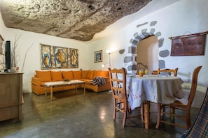 A cozy living room with a stone wall, a wooden dining table with chairs, a sofa, and a painting on the wall. - Rustic Country Estate with Pool (Artenara)