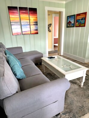 Ein Wohnzimmer mit grauem Sofa, einem Couchtisch aus Glas und Bildern an den Wänden.