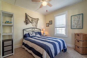 Ein Schlafzimmer mit einem Bett, einem Deckenventilator, einem Fenster mit Jalousien, einer Karte an der Wand und einem Regal mit Gegenständen.