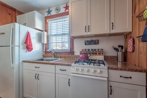Una cocina con armarios blancos, un hervidor rojo y una ventana con persianas.