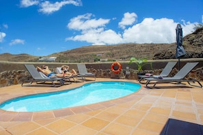 A swimming pool with lounge chairs and a lifebuoy, surrounded by a stone wall and a clear sky. - Stay with Pool & View (Artenara)