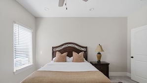 Een slaapkamer met een bed, een nachtkastje, een lamp, een raam met jaloezieën en een deur.