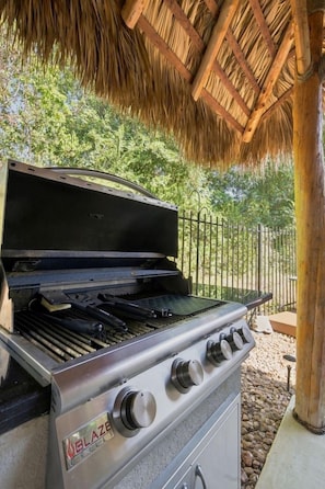 Una barbacoa exterior amb estructura metàl·lica, panell de control amb botons i teulada de palla.