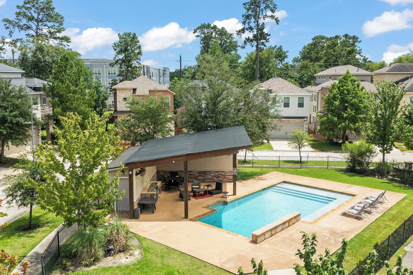 A residential area with a swimming pool, a covered patio with outdoor furniture, and a stone barbecue area.