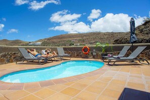 A swimming pool with lounge chairs and a lifebuoy, surrounded by a stone wall and a clear sky. - Lush Cave Home with Whirlpool (Artenara)