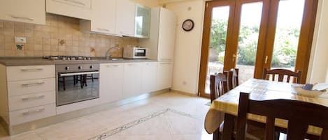 A kitchen with a stove, oven, microwave, and cabinets. There is a dining table with chairs and a window with a view of greenery.