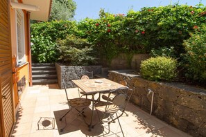 A patio with a table and chairs, a stone wall, and a staircase leading to an upper level. - Garden Apartment for 5 Guests (Trecastagn)