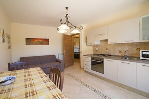 A compact kitchen with a dining area, a sofa, and a painting on the wall. - Garden Apartment for 5 Guests (Trecastagn)