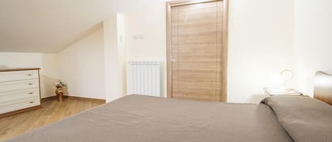A bedroom with a bed, a dresser, a radiator, and a door.