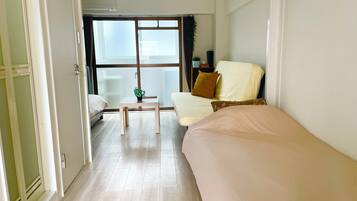 A hotel room with a bed, a small table with a plant, a window with curtains, and a bedside table with a lamp.