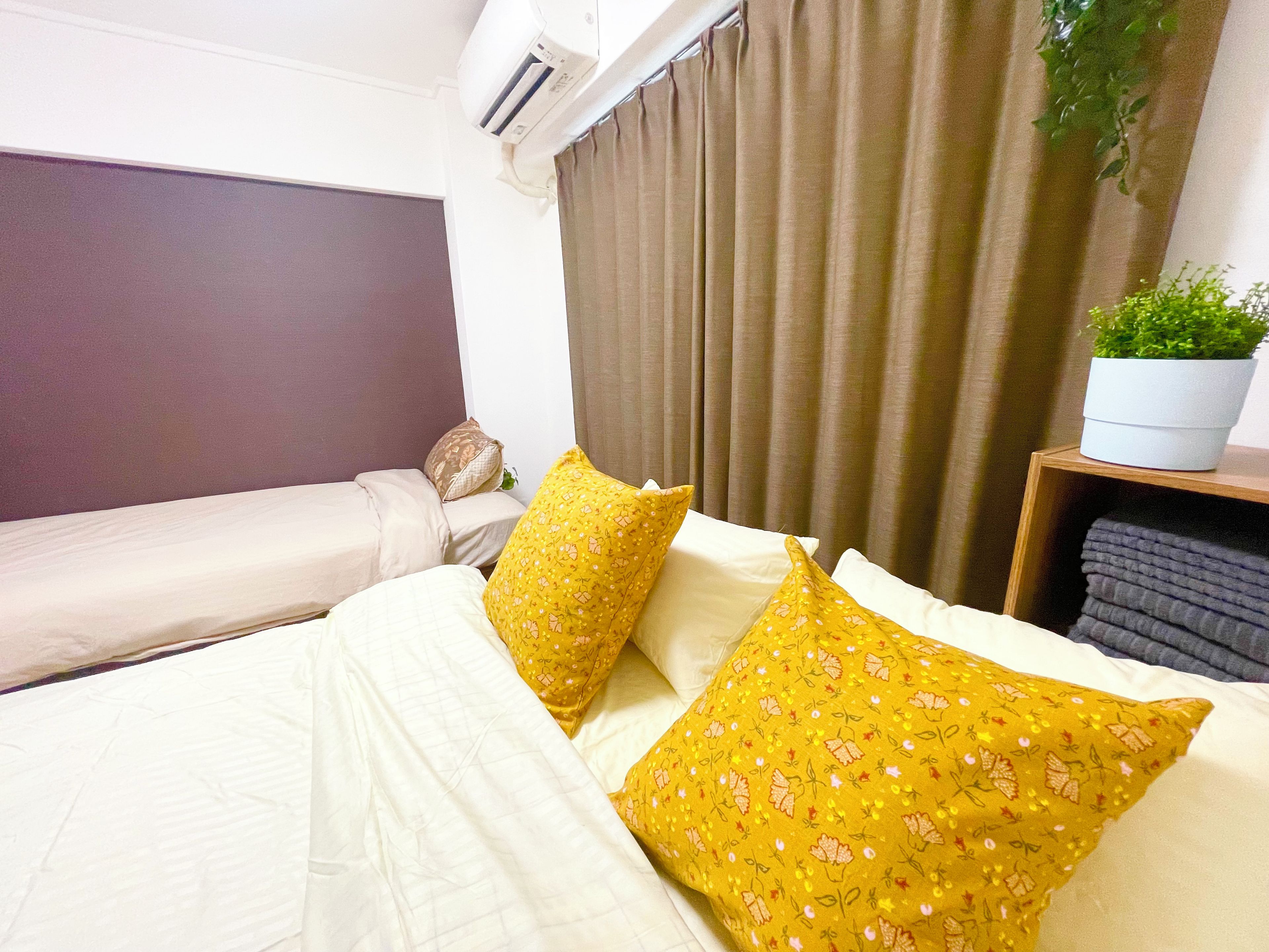 A hotel room with a bed, a bedside table with a plant, and a window with curtains.