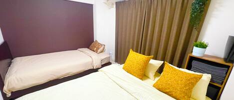 A hotel room with a bed, a bedside table with a plant, and an air conditioning unit.