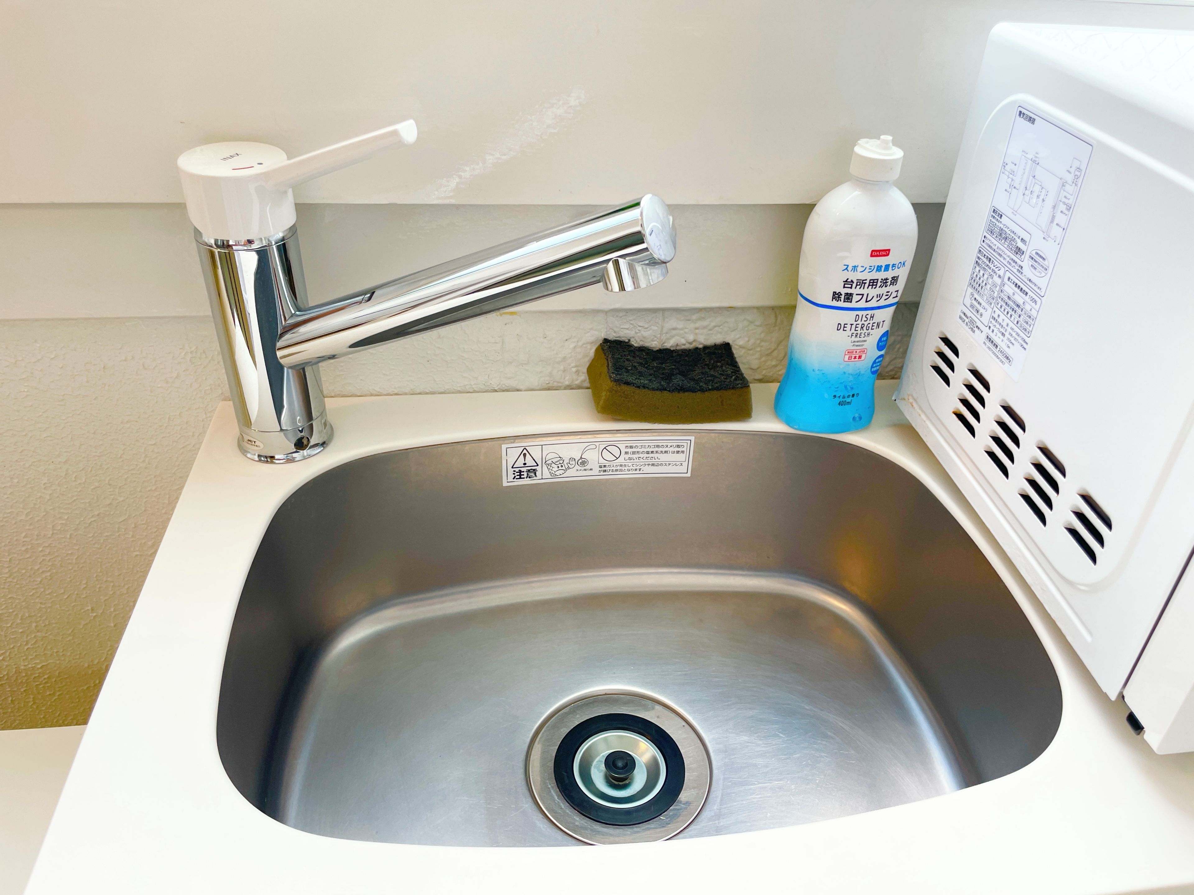 A stainless steel sink with a chrome faucet, a dish detergent bottle, and a sponge.