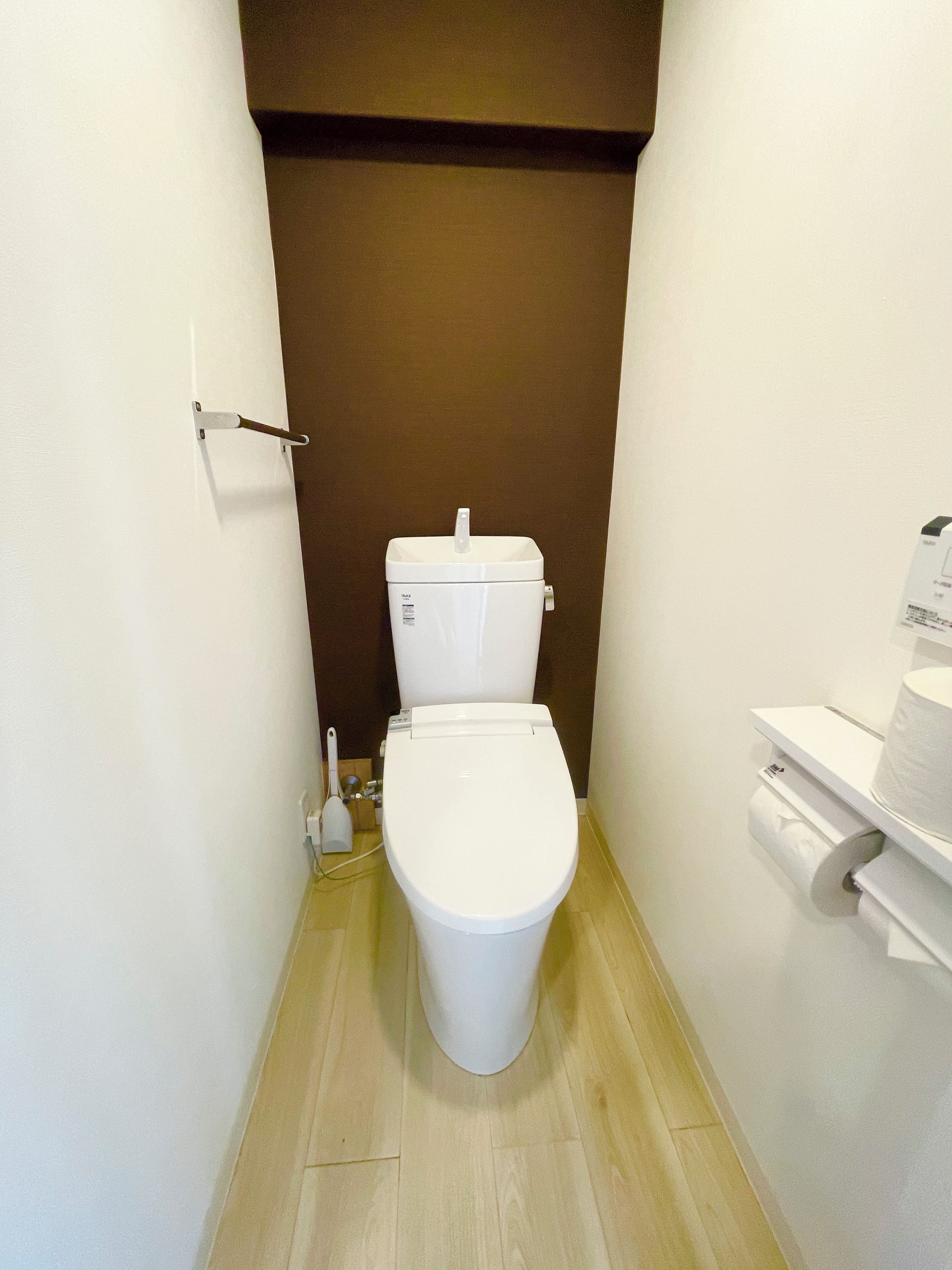 A small, narrow bathroom with a white toilet, a toilet paper holder, and a brown wall.