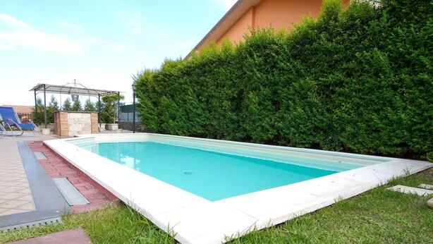 A rectangular swimming pool with a white edge, surrounded by grass and a hedge. - Spacious Sicilian Etna Villa (Trecastagni CT)