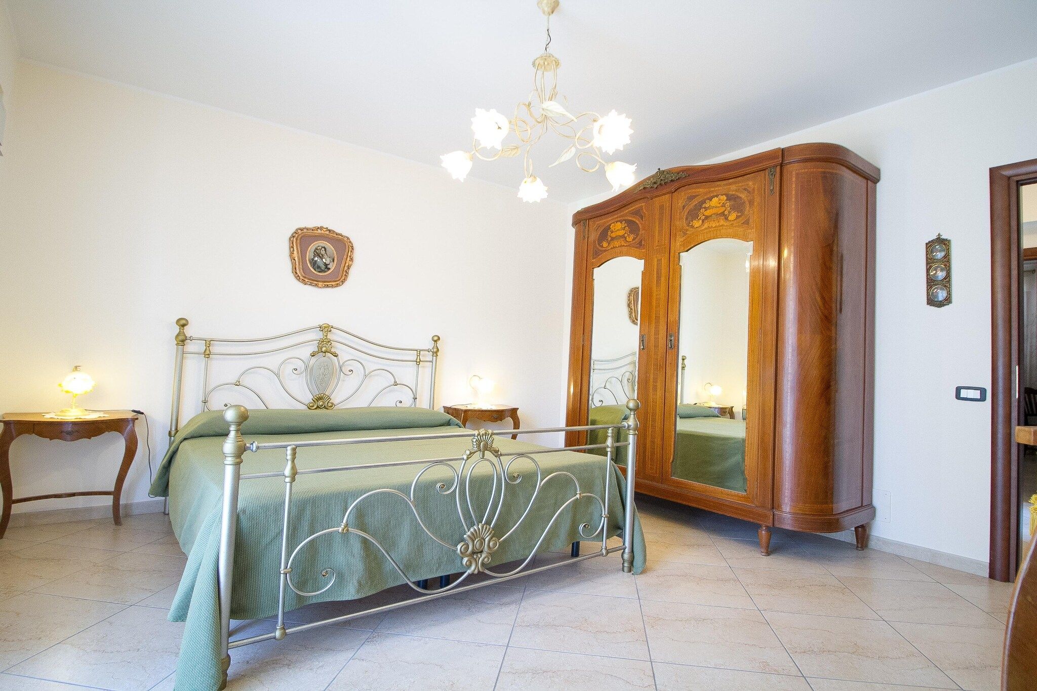 Ein Schlafzimmer mit einem Metallbett, einem Holzschrank, einem Spiegel und einer Chandelier.