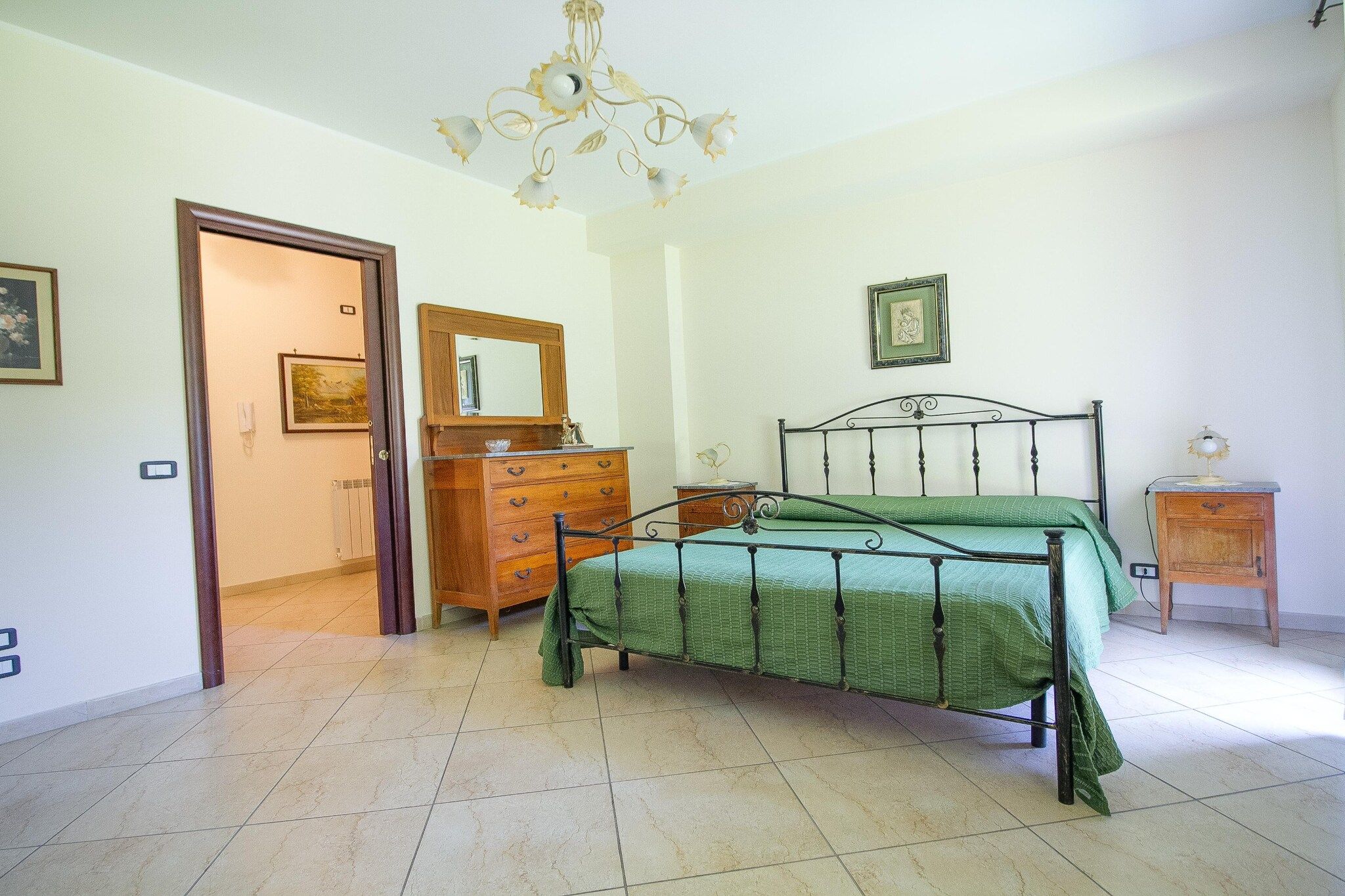 A bedroom with a bed, dresser, and a chandelier.