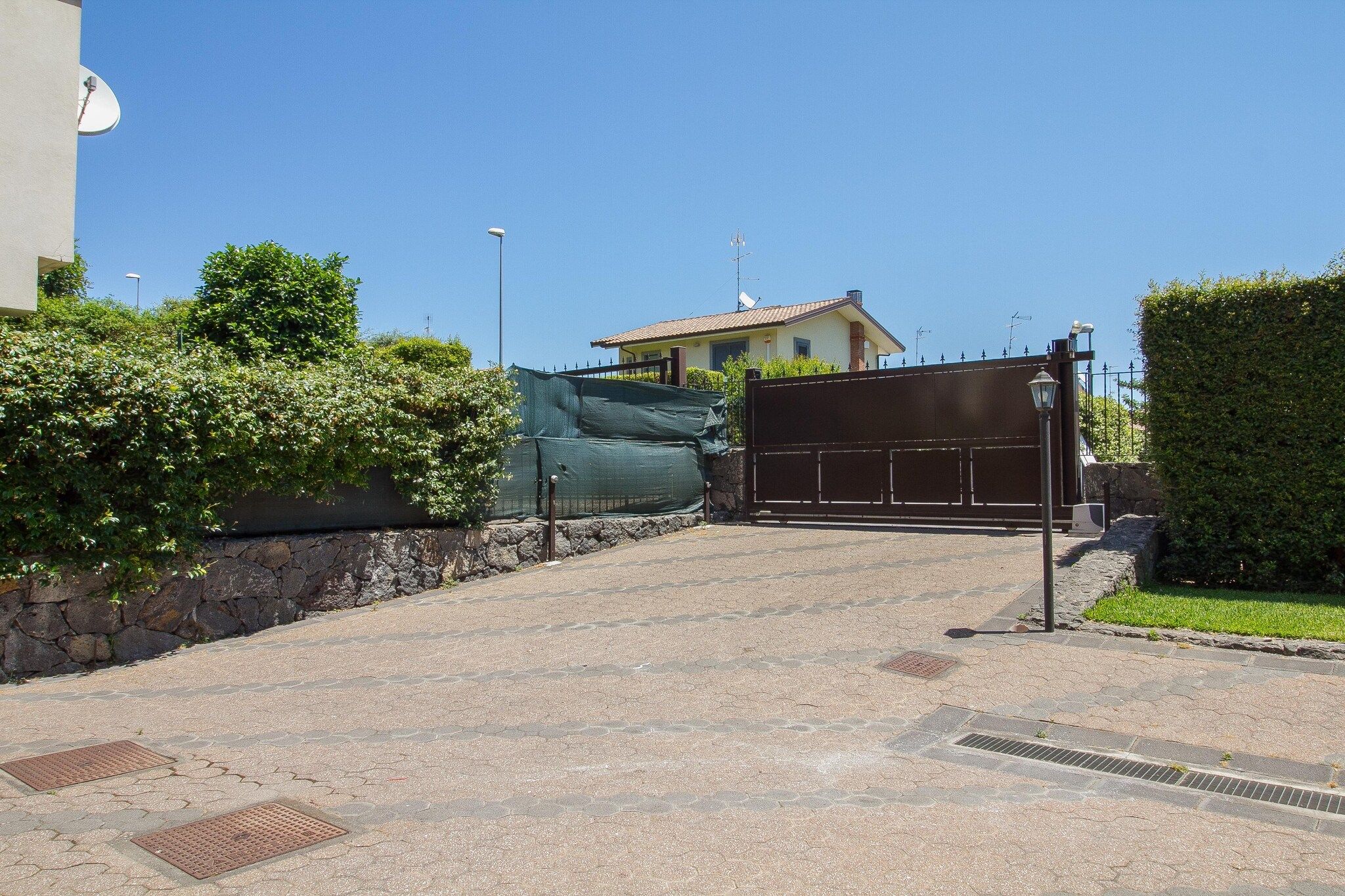 A paved driveway leading to a gated entrance with a house in the background.