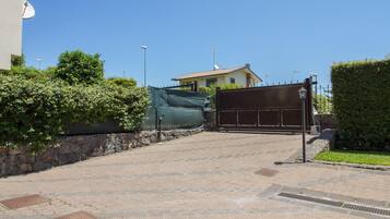 A paved driveway leading to a gated entrance with a house in the background.
