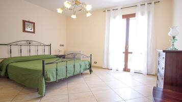 Een slaapkamer met een bed, een kroonluchter, een raam met gordijnen en een dressoir.