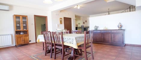Un coin repas avec une table dressée pour quatre personnes, entourée de chaises. On y trouve un meuble avec des portes en verre et un radiateur au mur.