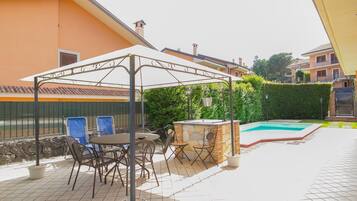 An outdoor patio with a covered seating area, a pool, and a stone wall.