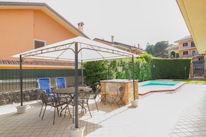 An outdoor patio with a covered seating area, a pool, and a stone wall.